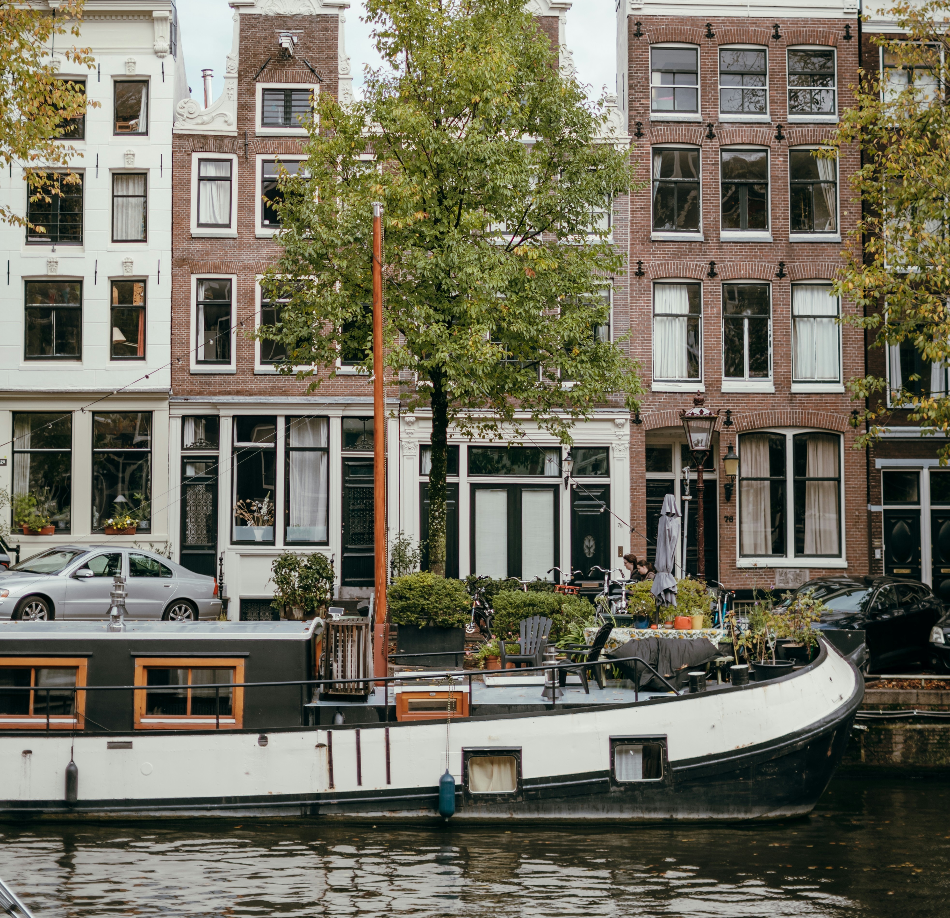 Amsterdam canal houses behind a moored houseboat, with autumn trees and water in the foreground
