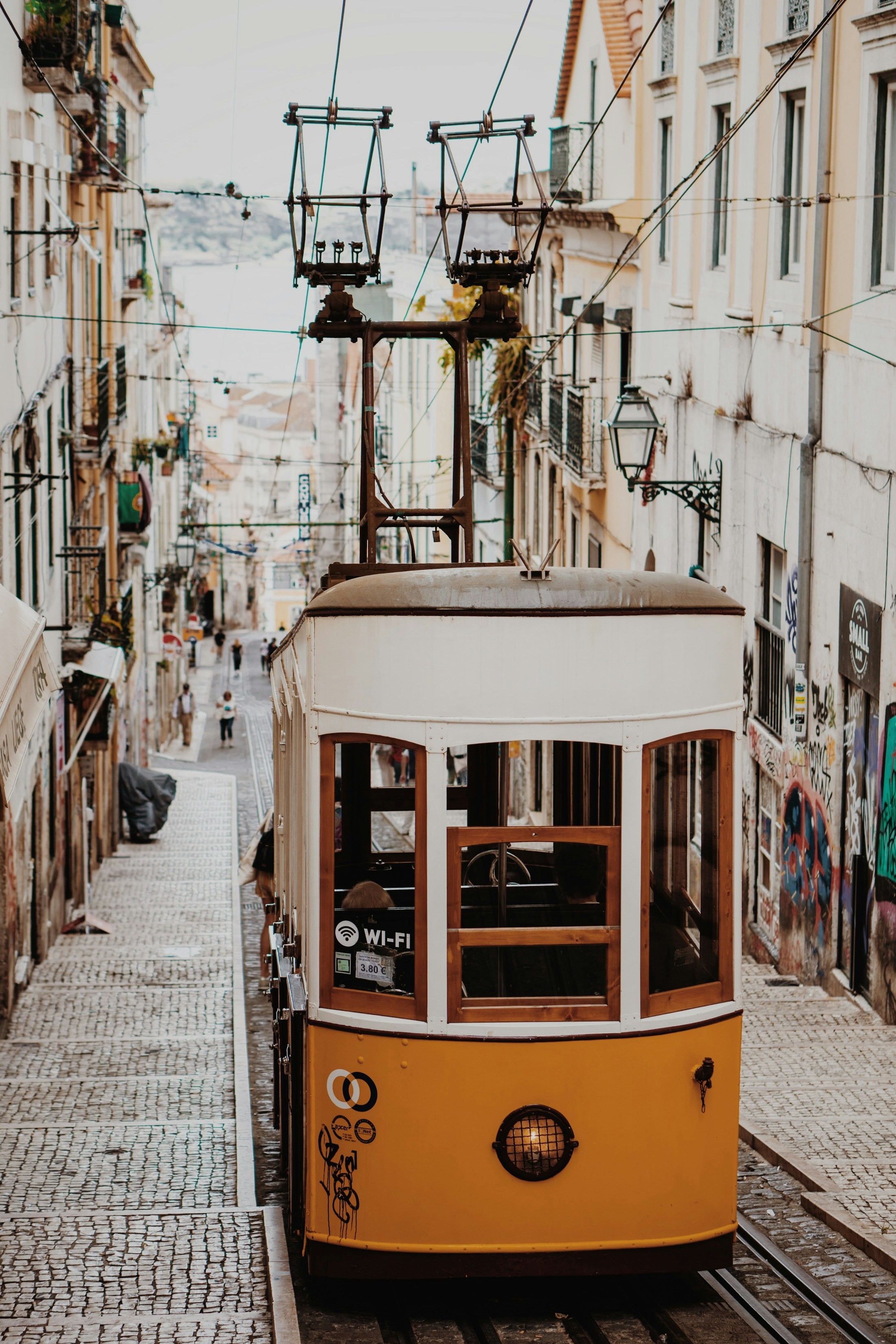 A yellow and white tram on a narrow Lisbon street framed by pale stone buildings